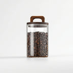 Clear cylindrical glass storage jar with wooden handle lid on white background