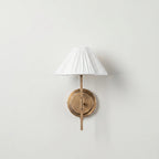 Pleated Fabric Wall Sconce – Brass Arm Wall Light with White Gathered Shade in a white studio. 