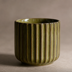 Green ceramic cup with ribbed texture on a beige background