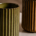 Two ceramic vases with ribbed texture, one green and one brown, on a neutral background.