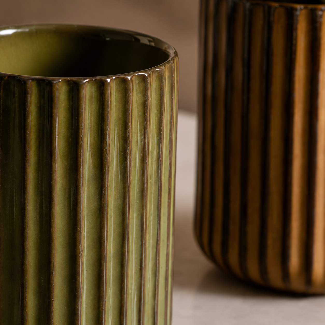 Two ceramic vases with ribbed texture, one green and one brown, on a neutral background.