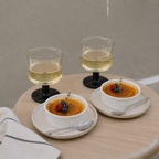 Two bowls of crème bréleé with glasses of white wine on a wooden table.