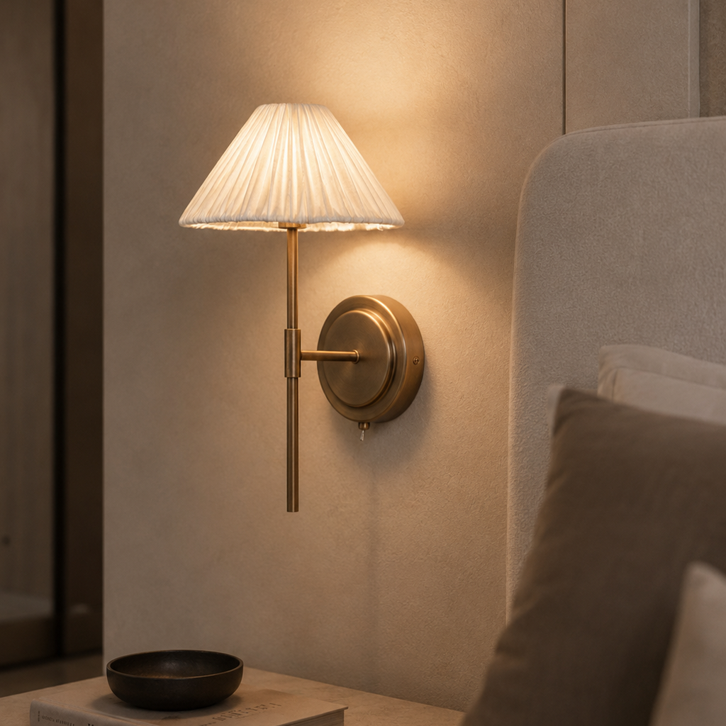 Wall-mounted lamp with pleated shade on a neutral wall next to a sofa.