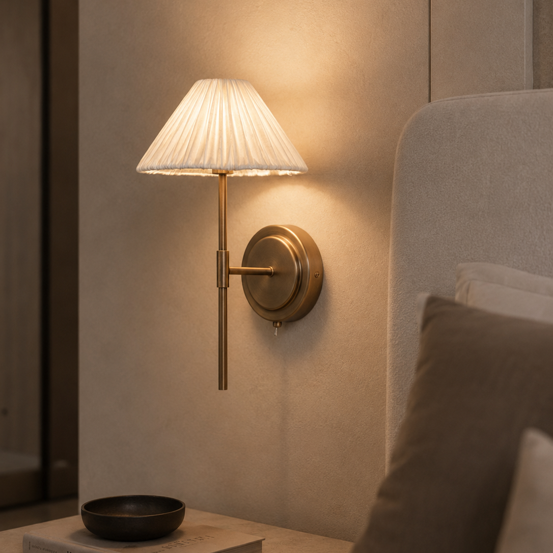 Wall-mounted lamp with pleated shade on a neutral wall next to a sofa.