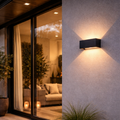 Modern outdoor wall light fixture on a concrete wall with a patio and living room interior.