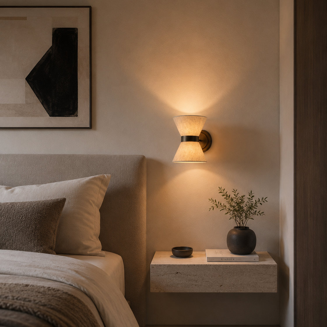 Modern bedroom with a wall-mounted light fixture, plant, and framed artwork.