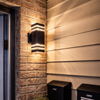 Outdoor wall lighting fixture on a stone wall with a plant and mailboxes below.