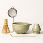Tea-making set with green ceramic bowl, whisk, and other tools on a white background