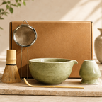 Tea-making set with green bowl, whisk, and other tools on a wooden surface.
