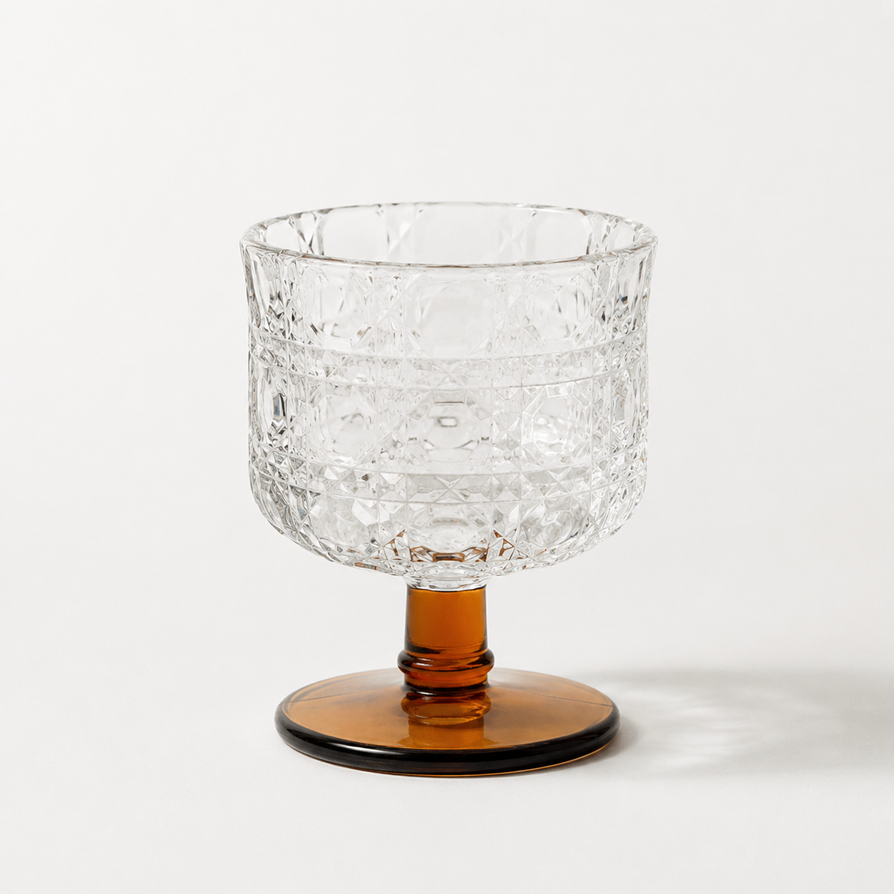 Clear glass bowl with textured surface and amber base on a white background
