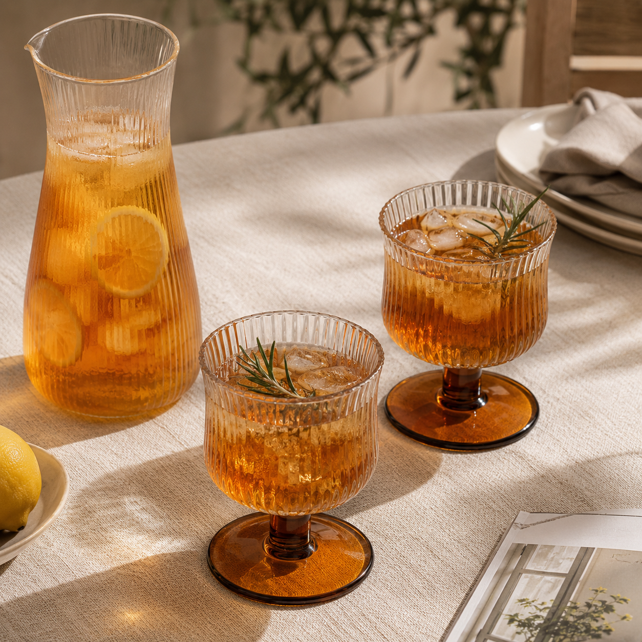 Two glasses of iced tea with lemon slices and rosemary garnishes on a tablecloth.