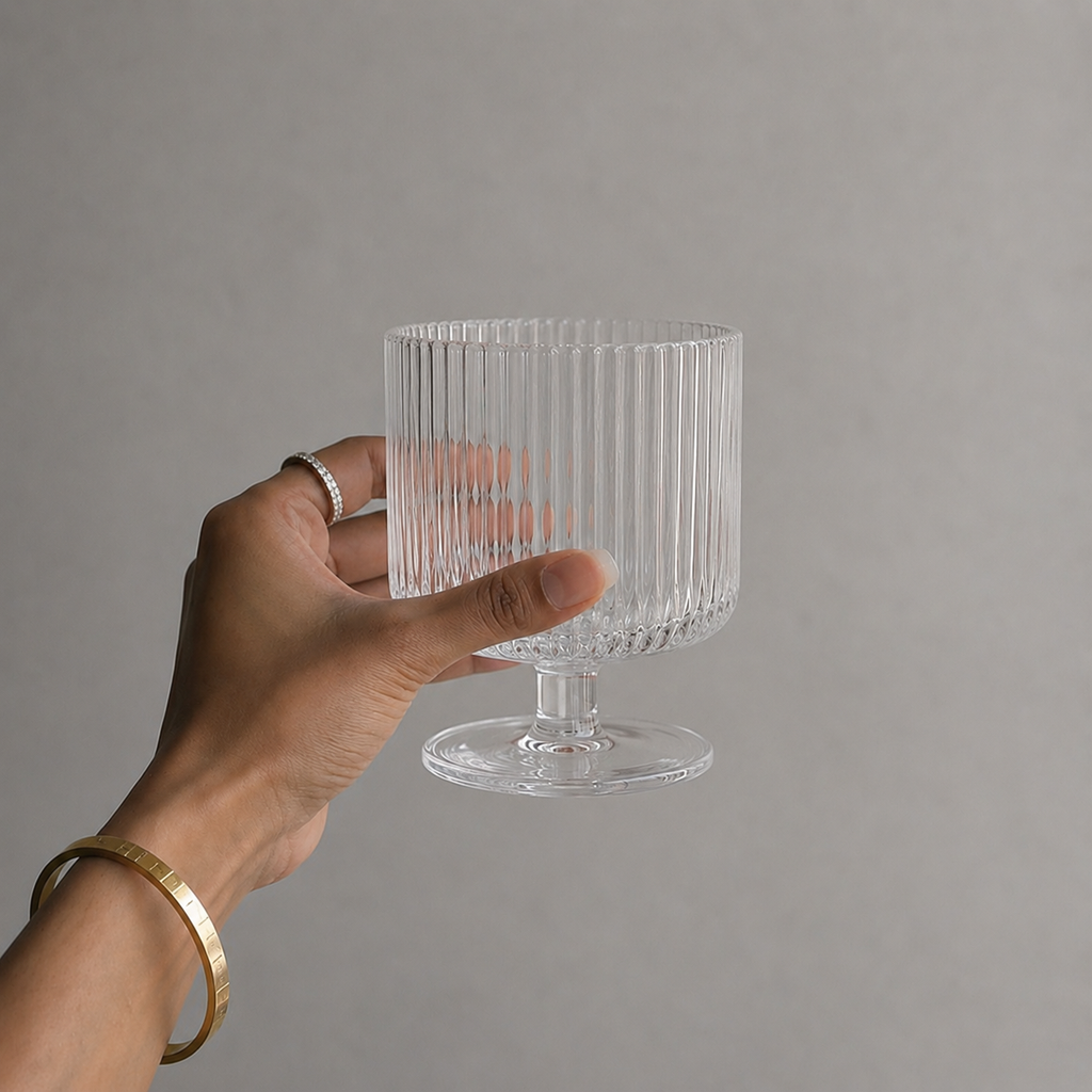 Hand holding a clear ribbed glass against a gray background