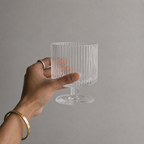 Hand holding a clear ribbed glass against a gray background