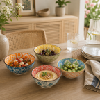 Colorful bowls with various dishes on a wooden table, with a blurred background of a room.