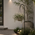 Hanging flower basket on a stand in a garden setting with a building in the background