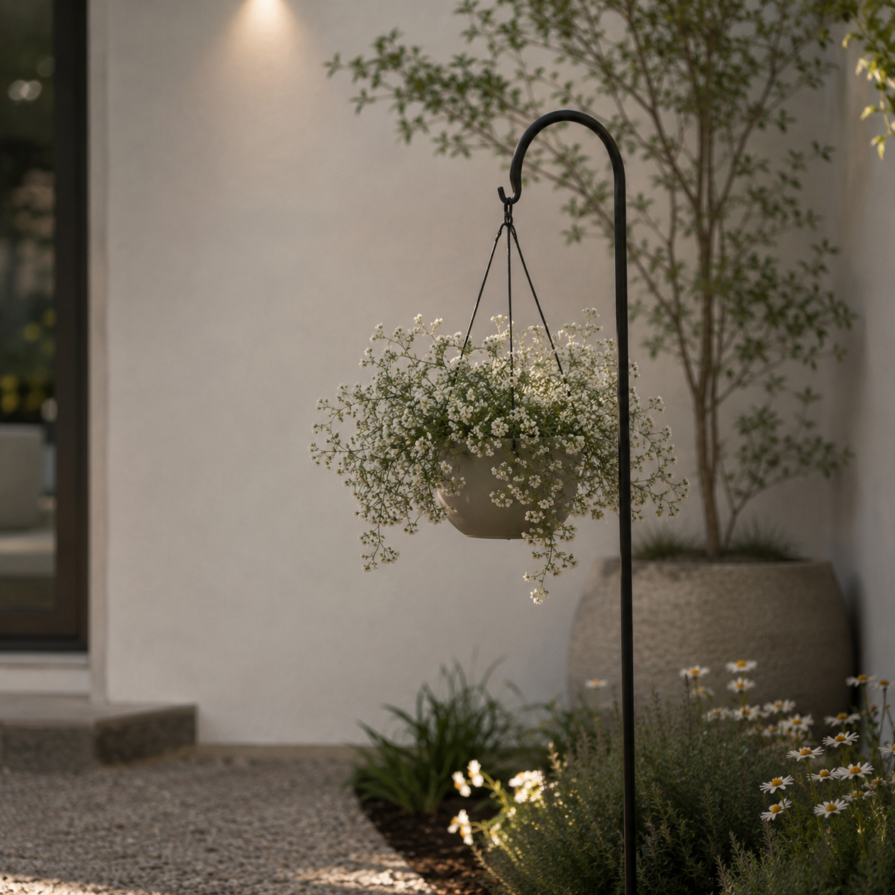 Hanging flower basket on a stand in a garden setting with a building in the background