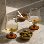 Two glasses of white wine with bowls of olives on a stone surface
