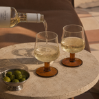White wine being poured into two glasses on a stone table with a bowl of olives.