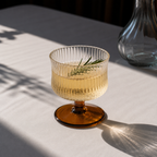 Glass with amber base and clear glass body on a light surface with a blurred background